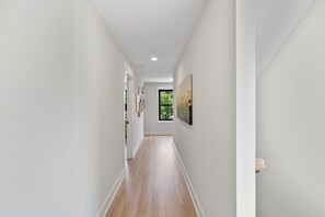 A narrow hallway with wooden flooring, white walls, and a window at the end. - Rooftop Retreat: Steps to Downtown Square (Murfreesboro)