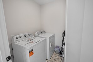A laundry room with two white Whirlpool washers and dryers, a tiled floor, and a door leading to another room. - Rooftop Retreat: Steps to Downtown Square (Murfreesboro)
