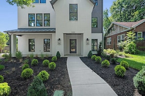 A two-story house with a number 520 on the front door, surrounded by a landscaped garden with various shrubs and a concrete pathway leading to the entrance. - Rooftop Retreat: Steps to Downtown Square (Murfreesboro)