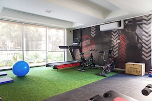 Een sportschool met trainingsapparatuur, een loopband, hometrainers en een blauwe fitnessbal.