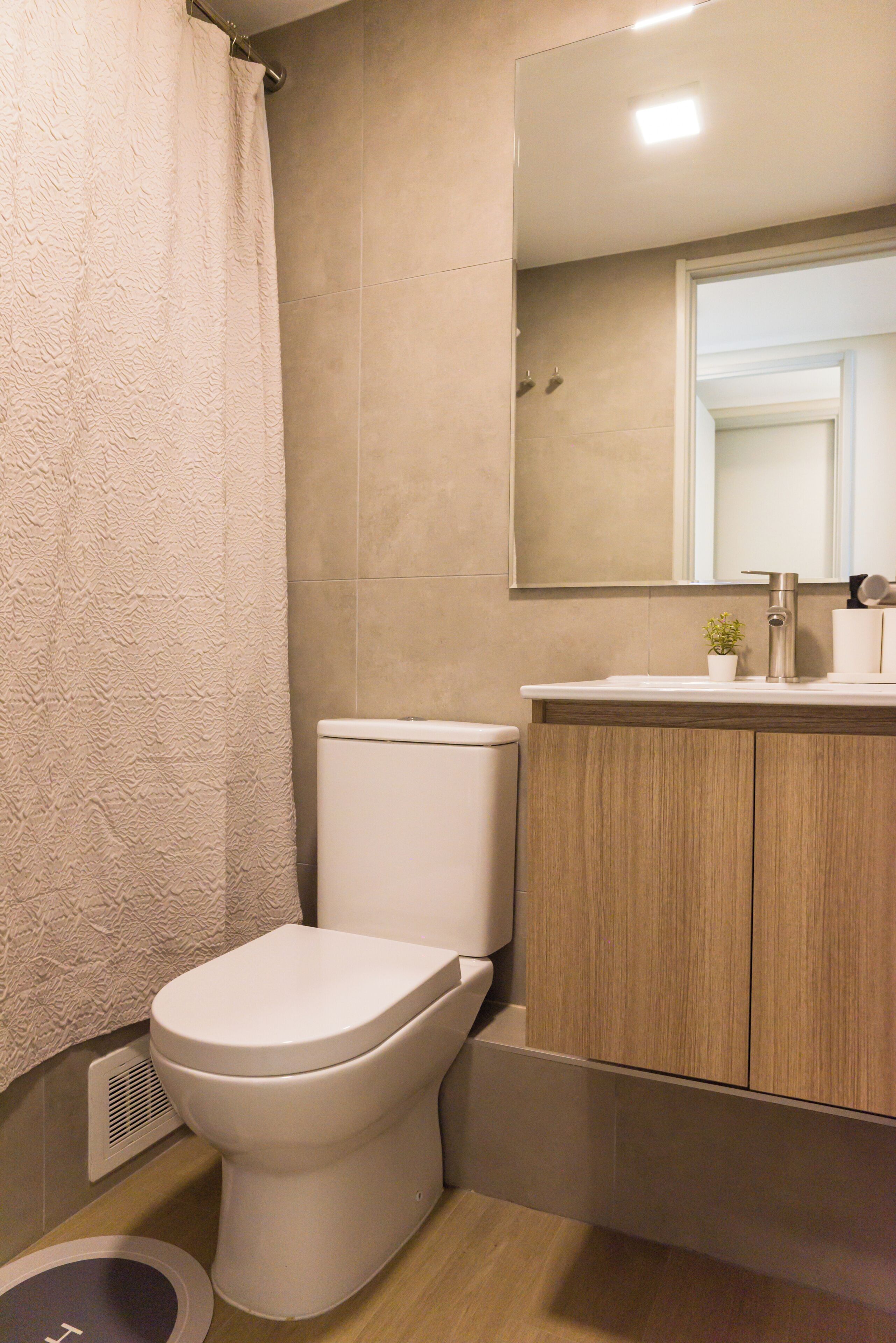 Et badeværelse med toilet, brusekabine, vask med spejl og skab.