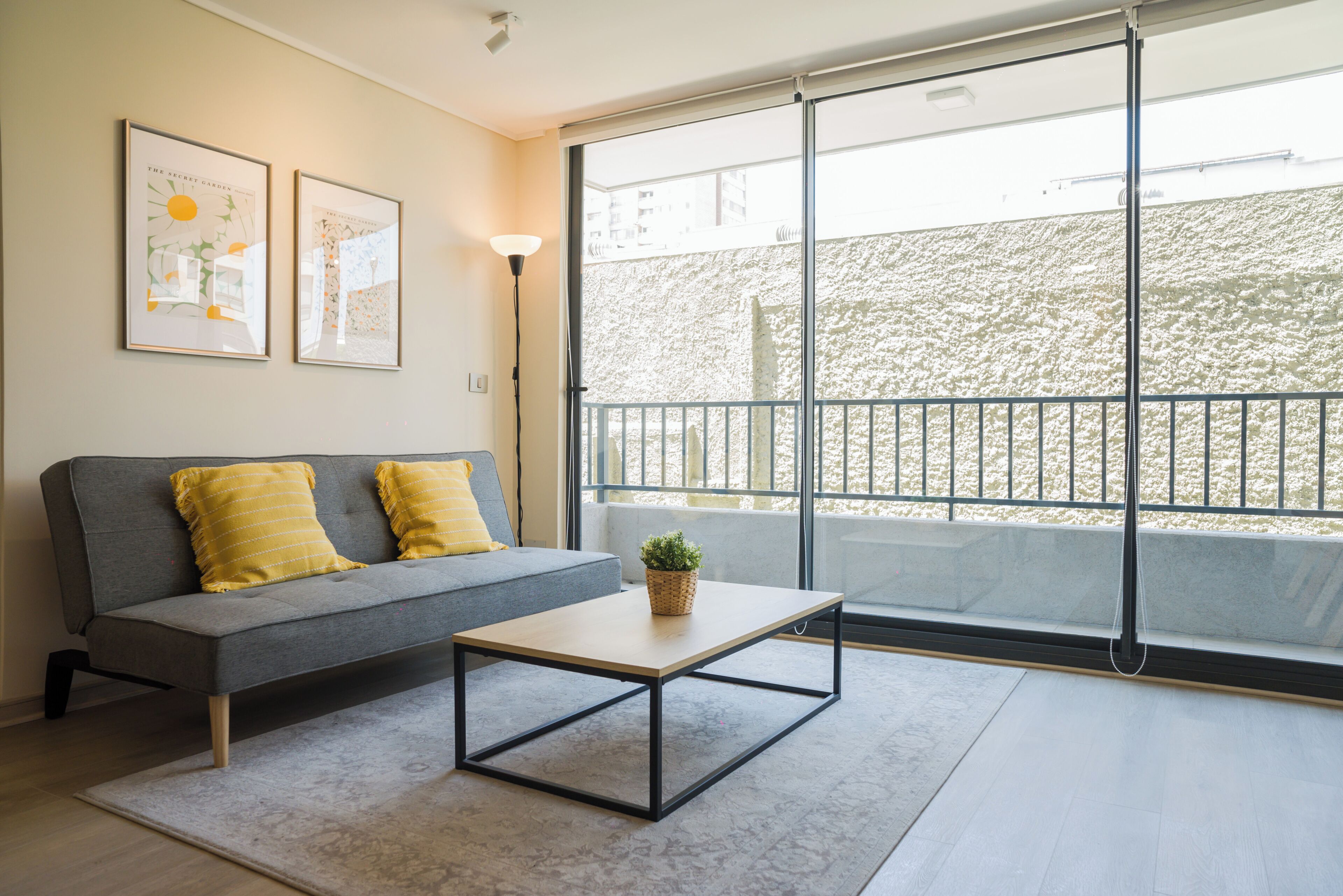 Un salon moderne avec un canapé gris, deux coussins jaunes, une petite table et une plante en pot.