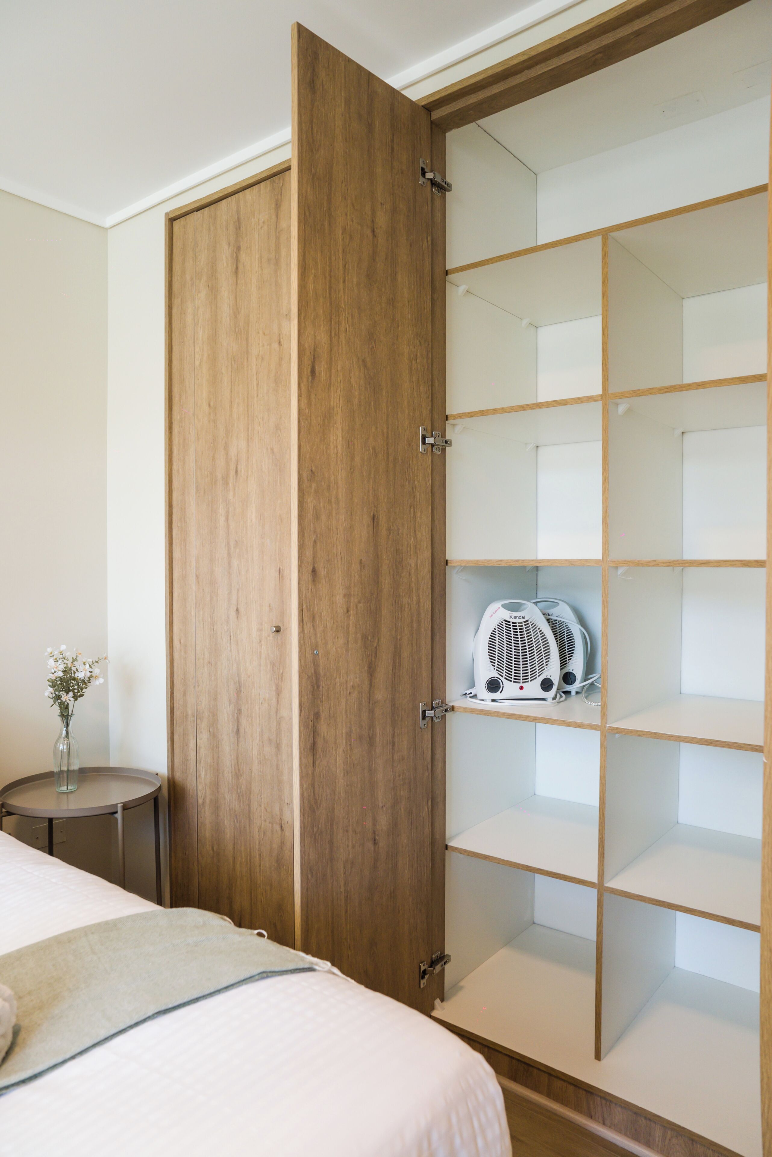 Een hotelkamer met een houten garderobe, een bed met een witte dekbedovertrek en een tafeltje met een bloemenvaas.