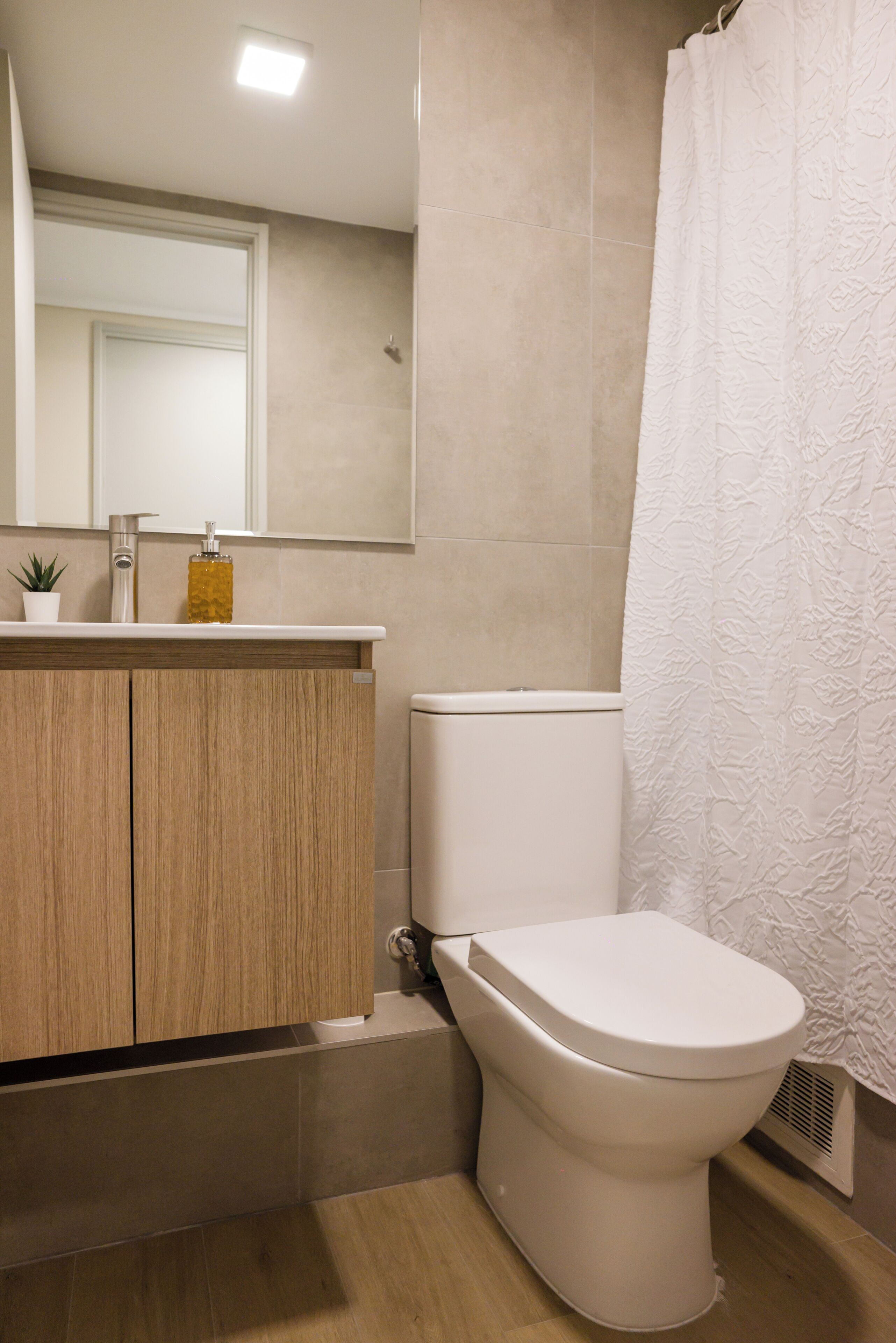 A bathroom with a toilet, a sink, a mirror, and a shower curtain.
