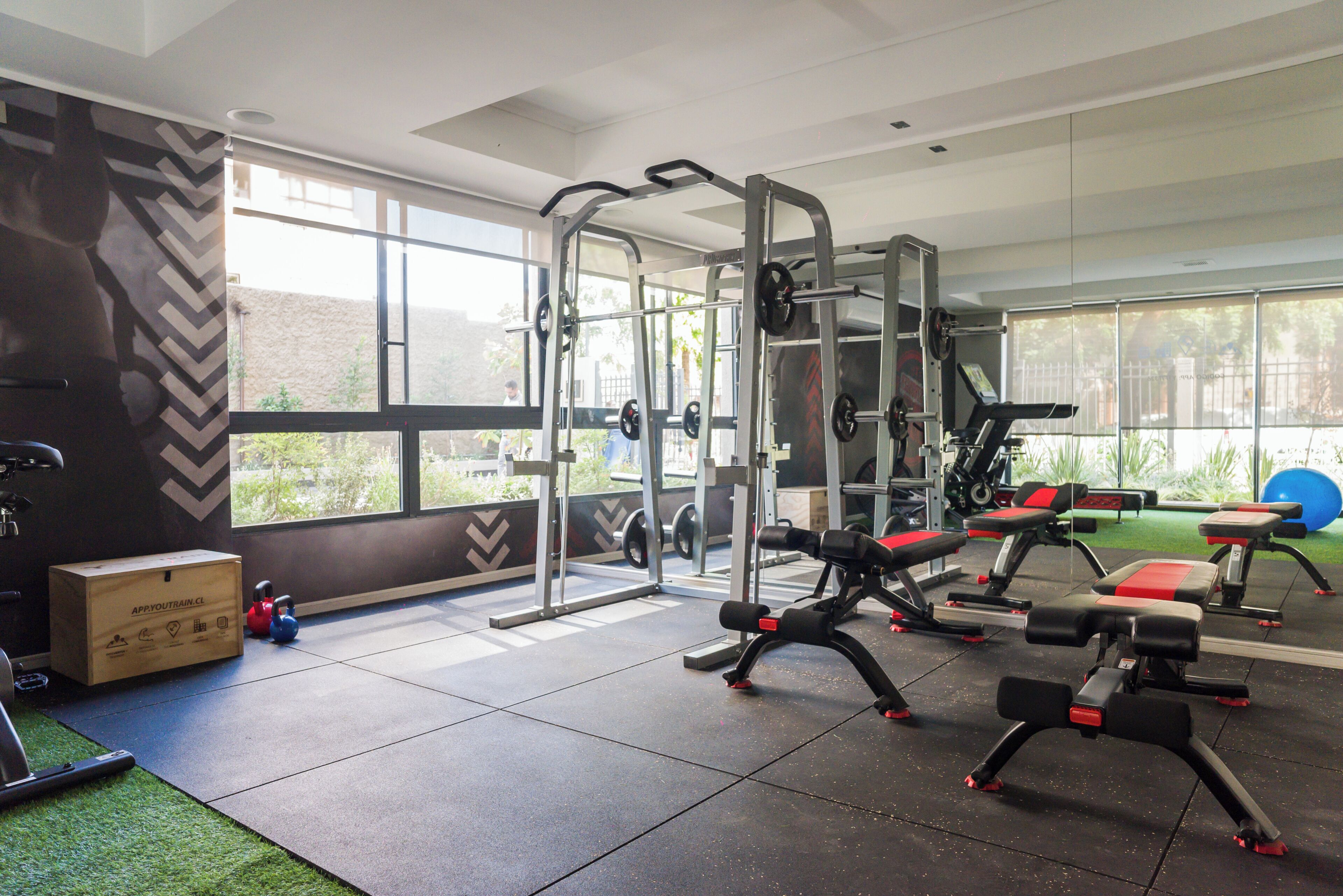 A gym with exercise equipment, a large window, and a green artificial turf area.