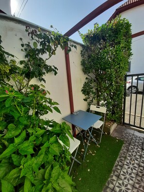 A small patio area with a table and chairs, surrounded by lush green plants and a white wall. - Duplex for 2 people in the St. Charles neighborhood, with a terrace overlooking the ocean and the golf course within walking distance (Biarritz)