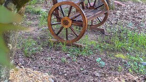 Eine Gartenbank aus Holz mit großen Rädern, platziert unter einem Baum in einer Grünanlage mit Rasen und Mulch als Bodengrund.
