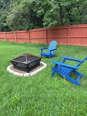 Ein Garten mit einem Feuerkorb, zwei blauen Adirondack-Stühlen und einem roten Holzzaun.