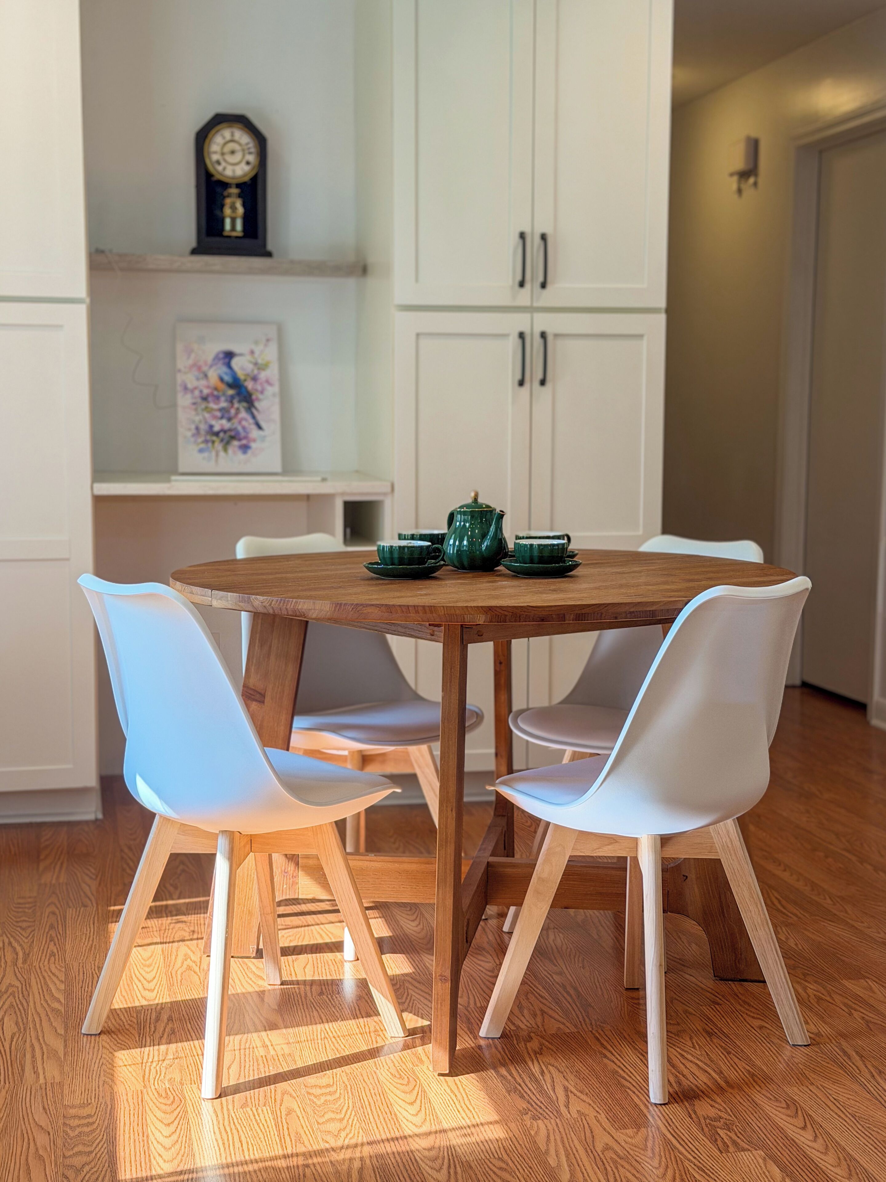 A dining area with a wooden table, white chairs, and a green teapot.