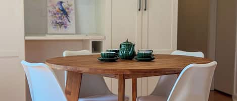 A dining area with a wooden table, white chairs, and a green teapot.