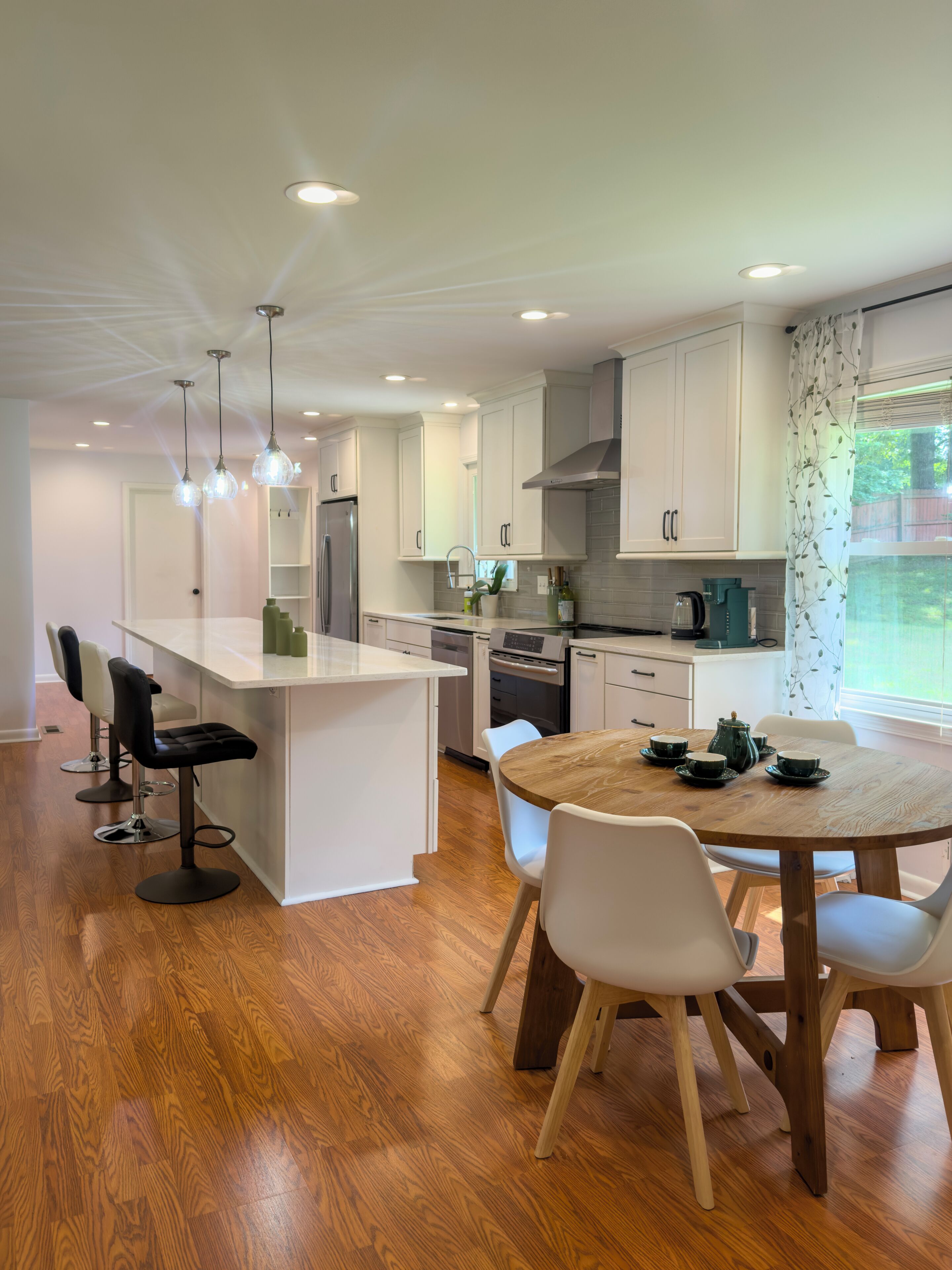 A modern kitchen with white cabinetry, a central island with bar stools, and a dining table set for four.