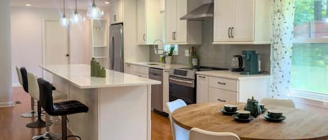 Une cuisine moderne avec des meubles blancs, un îlot central doté de tabourets de bar et une table à manger pour quatre personnes.