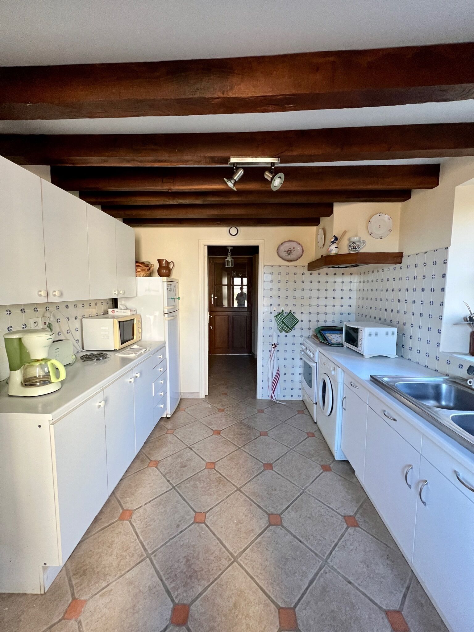 A kitchen with white cabinets, a tiled floor, and a wooden ceiling beam.