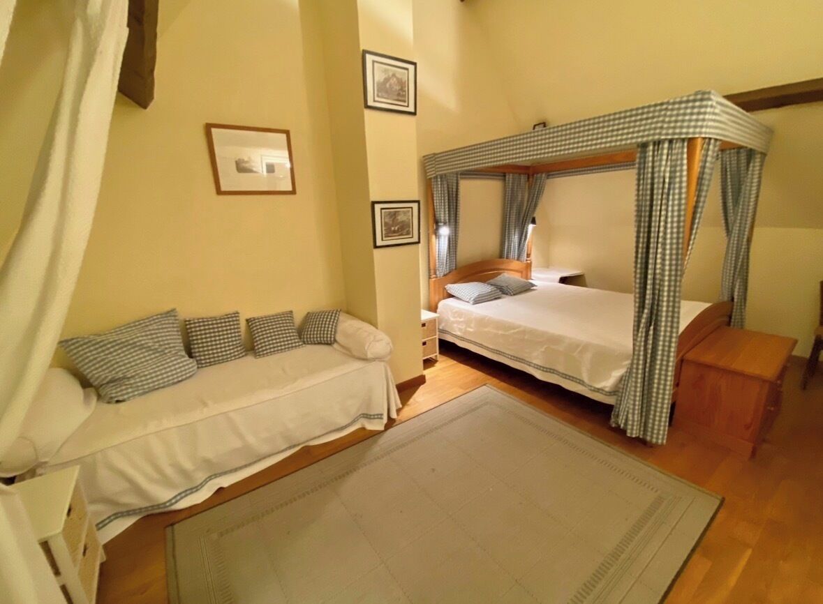 Een slaapkamer met een hemelbed, een slaapbank en een klein nachtkastje.