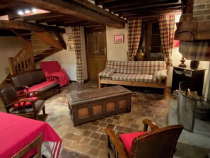 Een gezellige woonkamer met een bank, stoelen, een houten bankje en een trap.