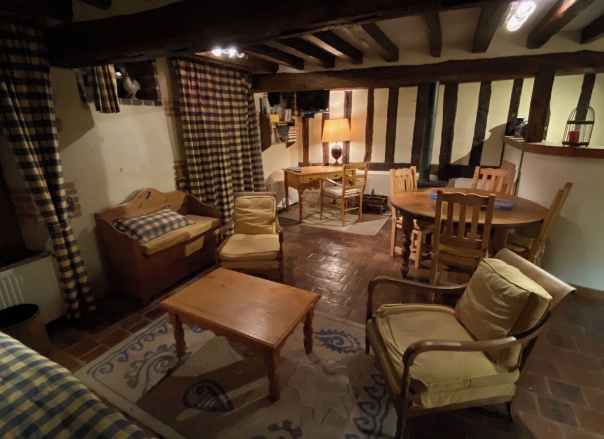 A cozy room with a wooden table, two sofas, and a chair. There is a lamp on a side table and a window with curtains.