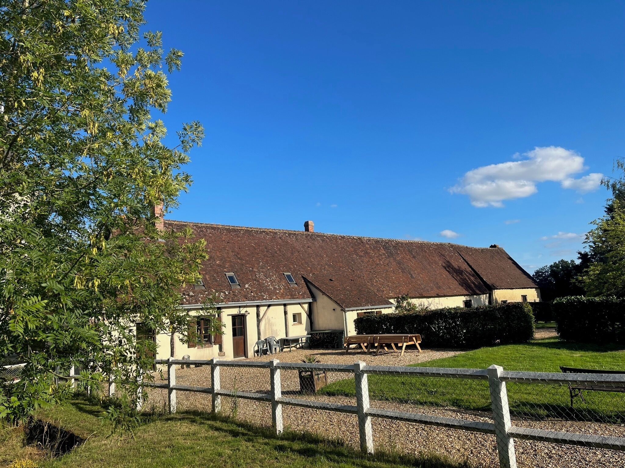 A farmstead with a large barn, a fenced area, and a picnic table.