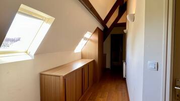 Un couloir étroit au plancher en bois, un plafond en pente doté de lucarnes et une porte sur le côté droit.