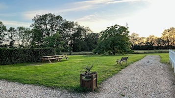 A grassy outdoor area with a gravel path, a wooden bench, and a picnic table.