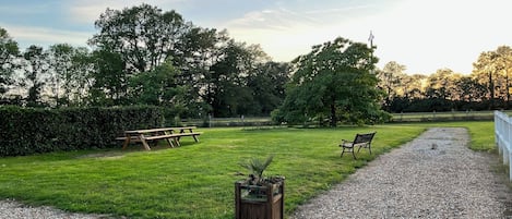 Ein grünes Freigelände mit Kiesweg, einer Holzbank und einem Picknicktisch.
