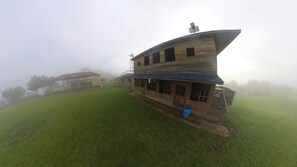 Een houten gebouw in rustieke stijl met een gebogen dak, een overdekt terras en een gazon.