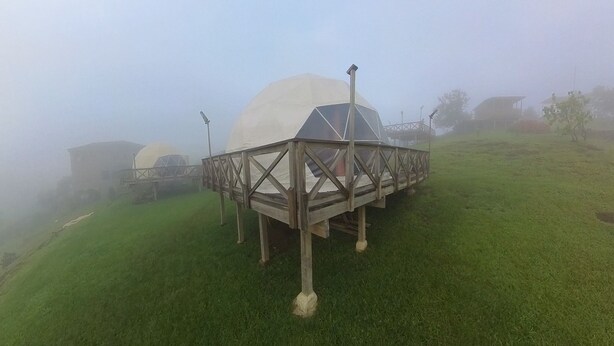 A dome-shaped structure with a wooden framework, situated on a grassy hill.