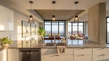 A modern kitchen with a granite countertop, stainless steel appliances, pendant lighting, and a view of the city through large windows.