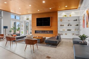 Un salon moderne doté d’un grand téléviseur à écran plat fixé au mur, d’une cheminée et de différents types de sièges, notamment des canapés et des fauteuils.