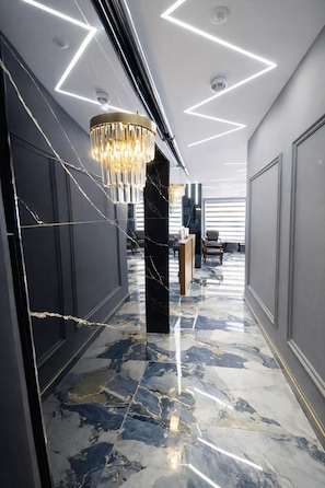 Un couloir doté d’un sol en marbre, d’un lustre et de luminaires au plafond aux formes géométriques.