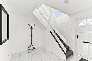 Un intérieur blanc avec un escalier, un porte-manteau et une porte.