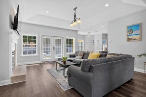 A spacious living room with a grey sectional sofa, a coffee table, and a TV mounted on the wall. - 3BR Pool Home/Close to Beaches/Mayo/UNF/Towncenter (Jacksonville)
