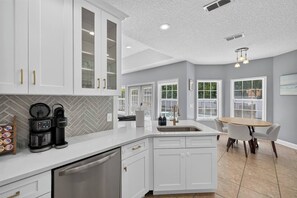 A modern kitchen with white cabinetry, a built-in dishwasher, and a coffee maker. - 3BR Pool Home/Close to Beaches/Mayo/UNF/Towncenter (Jacksonville)