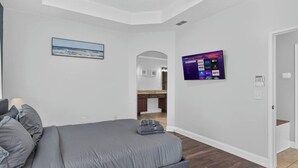 Ein Schlafzimmer mit einem Bett, einem an der Wand befestigten Fernseher und Blick zur Küche.