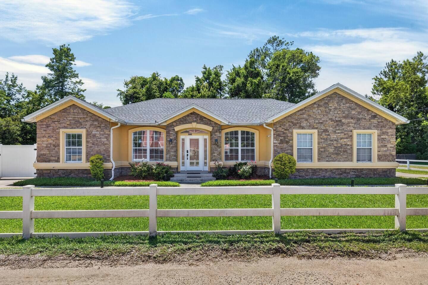 A two-story house with a stone facade, a front porch, and a white picket fence.