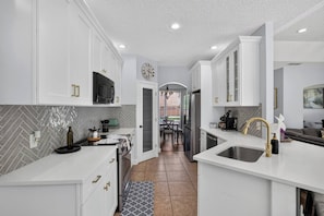 A modern kitchen with white cabinetry, a herringbone tile backsplash, stainless steel appliances, and a patterned rug. - 3BR Pool Home/Close to Beaches/Mayo/UNF/Towncenter (Jacksonville)
