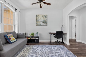 A living room with a gray sofa, a black office chair, a wooden desk, and a patterned rug. - 3BR Pool Home/Close to Beaches/Mayo/UNF/Towncenter (Jacksonville)