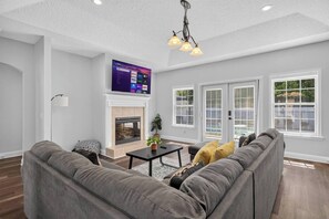 A modern living room with a fireplace, a large flat-screen TV, and a grey sectional sofa. - 3BR Pool Home/Close to Beaches/Mayo/UNF/Towncenter (Jacksonville)