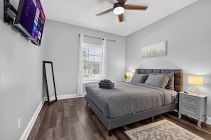 A bedroom with a bed, nightstands, a ceiling fan, a TV mounted on the wall, and a window with blinds. - 3BR Pool Home/Close to Beaches/Mayo/UNF/Towncenter (Jacksonville)