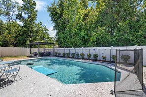 Una piscina rectangular con un área de descanso sombreada y una cerca.