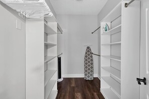 Un couloir étroit, avec des étagères blanches de part et d’autre, un objet cylindrique noir sur la gauche et une planche à repasser à motifs sur la droite.