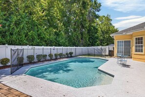 A rectangular swimming pool with a white fence and a patio area with a table and chairs. - 3BR Pool Home/Close to Beaches/Mayo/UNF/Towncenter (Jacksonville)