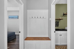 A hallway with a white door, a bench with a wooden top, and a kitchen area with a sink and cabinets. - 3BR Pool Home/Close to Beaches/Mayo/UNF/Towncenter (Jacksonville)