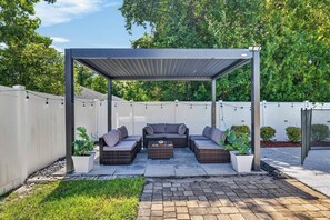 A covered outdoor seating area with a pergola, wicker furniture, and potted plants. - 3BR Pool Home/Close to Beaches/Mayo/UNF/Towncenter (Jacksonville)