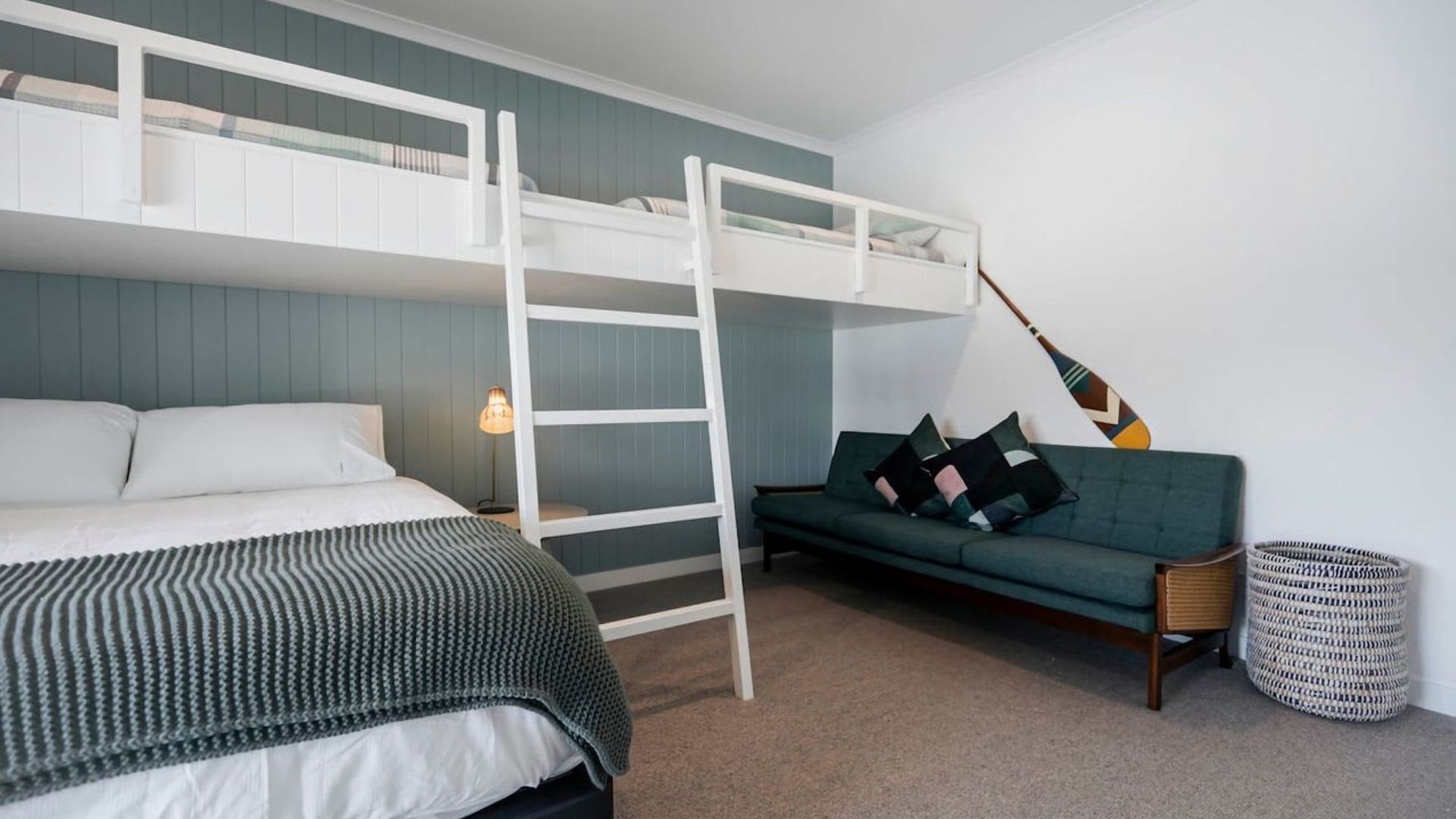 A bunk bed with a ladder, a sofa, a lamp, and a woven basket.