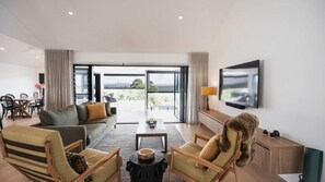 A modern living room with a sofa, chairs, a coffee table, and a TV. - Noosa Sunsets - Luxury Home with Stunning Views (Noosa Heads)