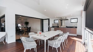 Cocina moderna con extractor de acero inoxidable, comedor con mesa y sillas blancas, y terraza de madera.