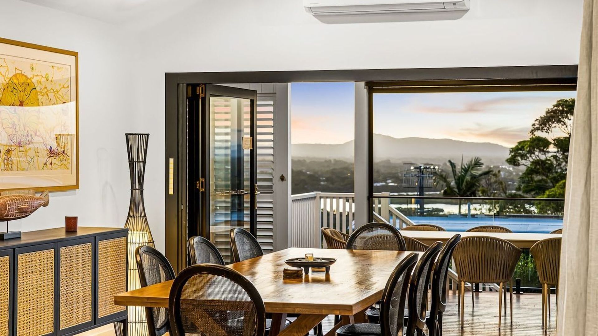Ein Essbereich mit Tisch und Stühlen, ein großes Fenster mit Blick auf einen Pool und Berge, sowie ein gerahmtes Kunstwerk an der Wand.