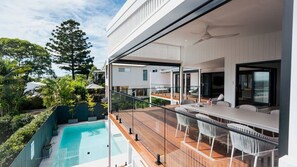 A modern outdoor deck with a pool, dining area, and a view of the surrounding greenery. - Noosa Sunsets - Luxury Home with Stunning Views (Noosa Heads)