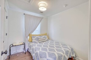 Une chambre à coucher avec un lit, une table de chevet, une lampe et une fenêtre avec des rideaux.