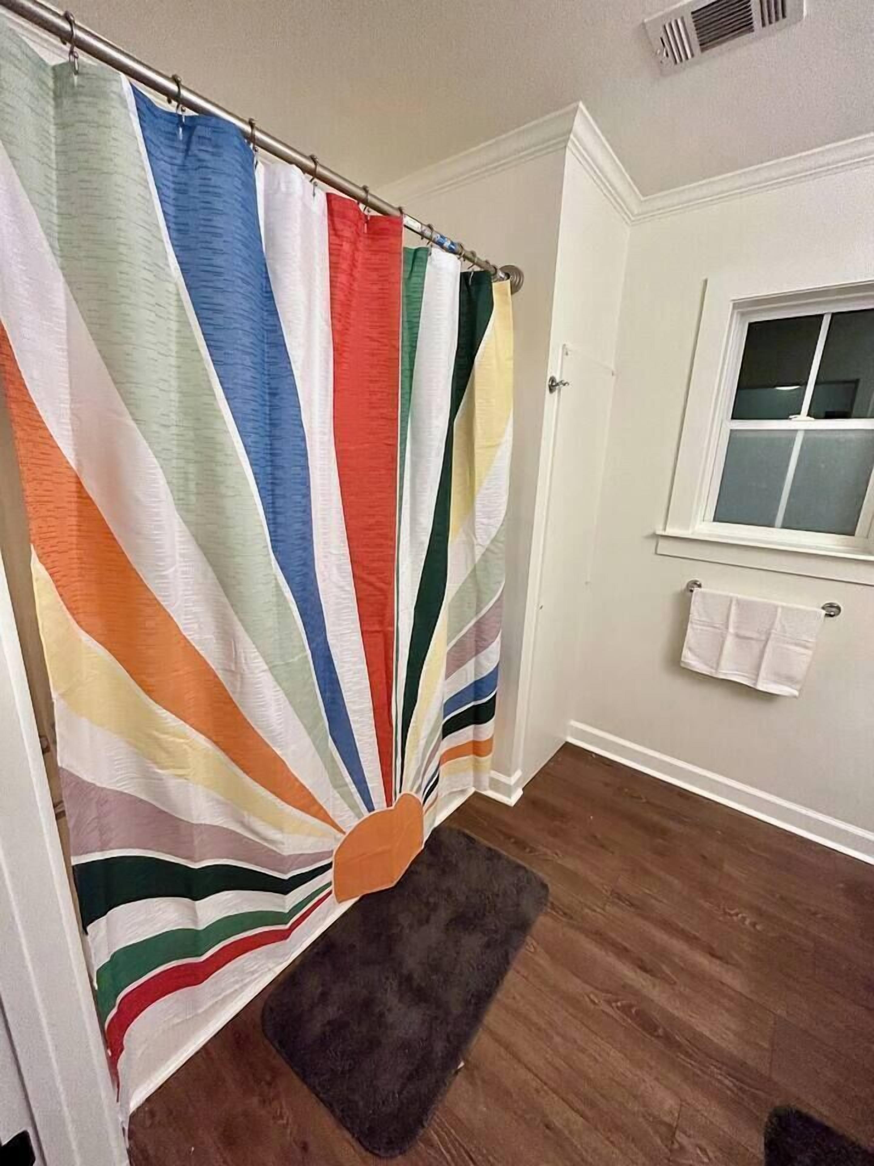 A bathroom with a shower curtain featuring a striped pattern, a window, and a towel rack.
